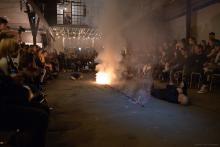 two bodies lying on the ground of a warehouse, a golden thread on fire with smoke between them